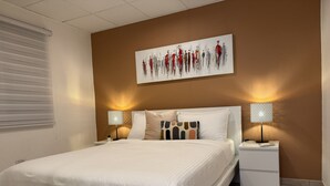 A modern bedroom with a large bed, two bedside tables, a wall-mounted artwork, and two wall lamps. - Modern 3BR Home in Fontana Village with Power & Water Backup (Carolina)