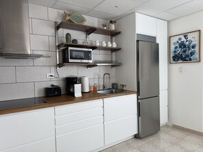 Una cucina moderna con un frigorifero in acciaio inossidabile, scaffali in legno e un forno a microonde.