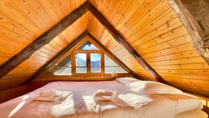A cozy attic bedroom with a wooden sloped ceiling, a large bed with pillows, and a window offering a mountain view. - Rustico Caterina - Corippo, Corippo, Val Verzasca, Switzerland (Corippo, Val Verzasca)
