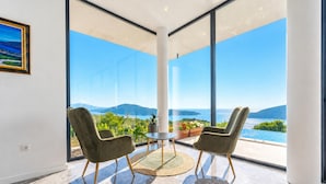 A modern room with a large window, two chairs, a small table, and a potted plant.
