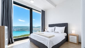 A modern bedroom with a large bed, a nightstand, and a view of the sea.
