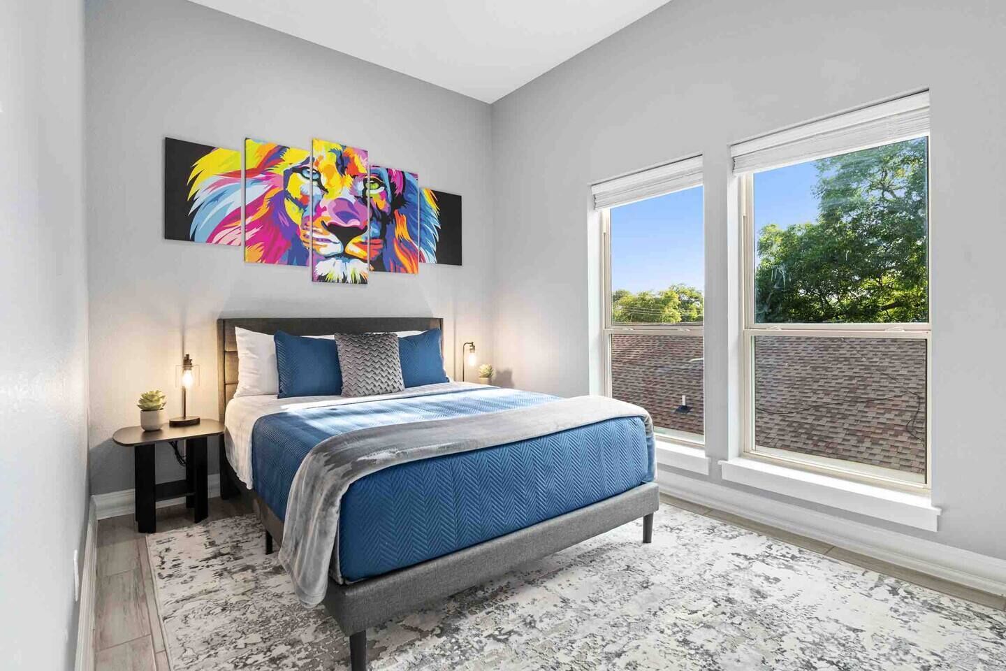 Un dormitorio con una cama, un ventanal grande y un cuadro abstracto y colorido sobre la cama.