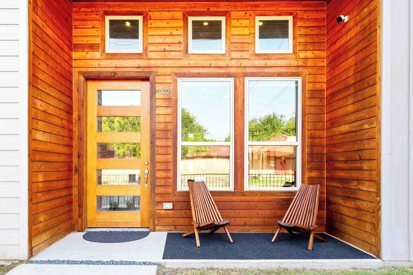 Une cabane en bois avec une porte d’entrée, deux fenêtres et deux chaises en bois à l’extérieur.