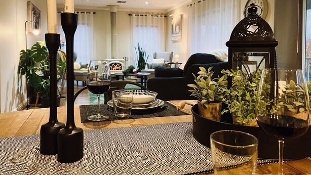 Ein gemütliches Wohnzimmer mit Kamin, einem Essplatz mit Kerzen, einem Weinglas und einem Blumentopf.