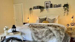 Ein Schlafzimmer mit einem Bett, Nachttischen, einer Lampe und einem an der Wand befestigten Regal mit Dekorationen.