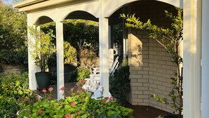 Ein überdachter Patio-Bereich mit Backsteinwand, Blumentöpfen und einer weißen Bank.