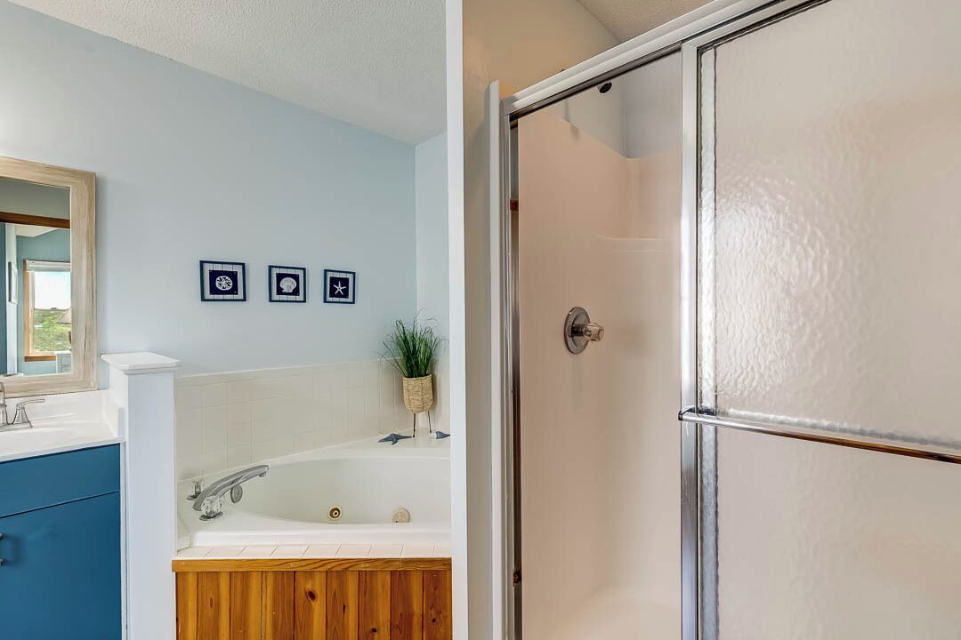 Une salle de bain avec une baignoire blanche, un meuble-lavabo en bois et un miroir. Trois tableaux encadrés sont accrochés au mur.
