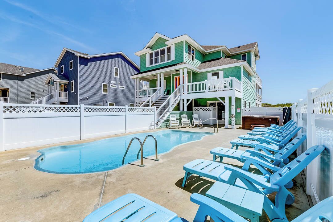 Une piscine avec des chaises longues et une maison à deux étages dotée d’un porche.
