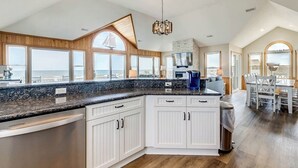 A spacious kitchen with a large island, wooden cabinetry, and a view of the ocean. - What the Shell | Oceanfront | Private Pool, Hot Tub, Community Pool (Corolla)