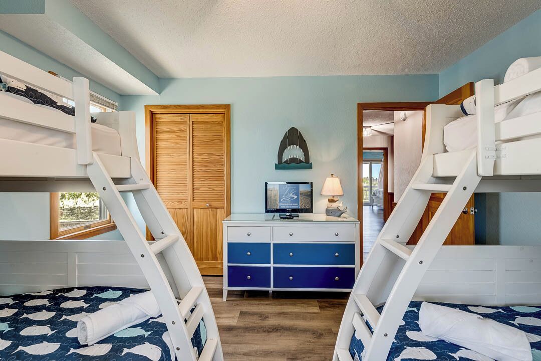 A bunk bed room with a wooden door, a dresser with drawers, a television, and a lamp.