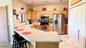 A kitchen with wooden cabinets, a central island with stools, a refrigerator, and a microwave. - Beautiful Mountain Views and a spacious relaxing home in NW Tucson. (Tucson)
