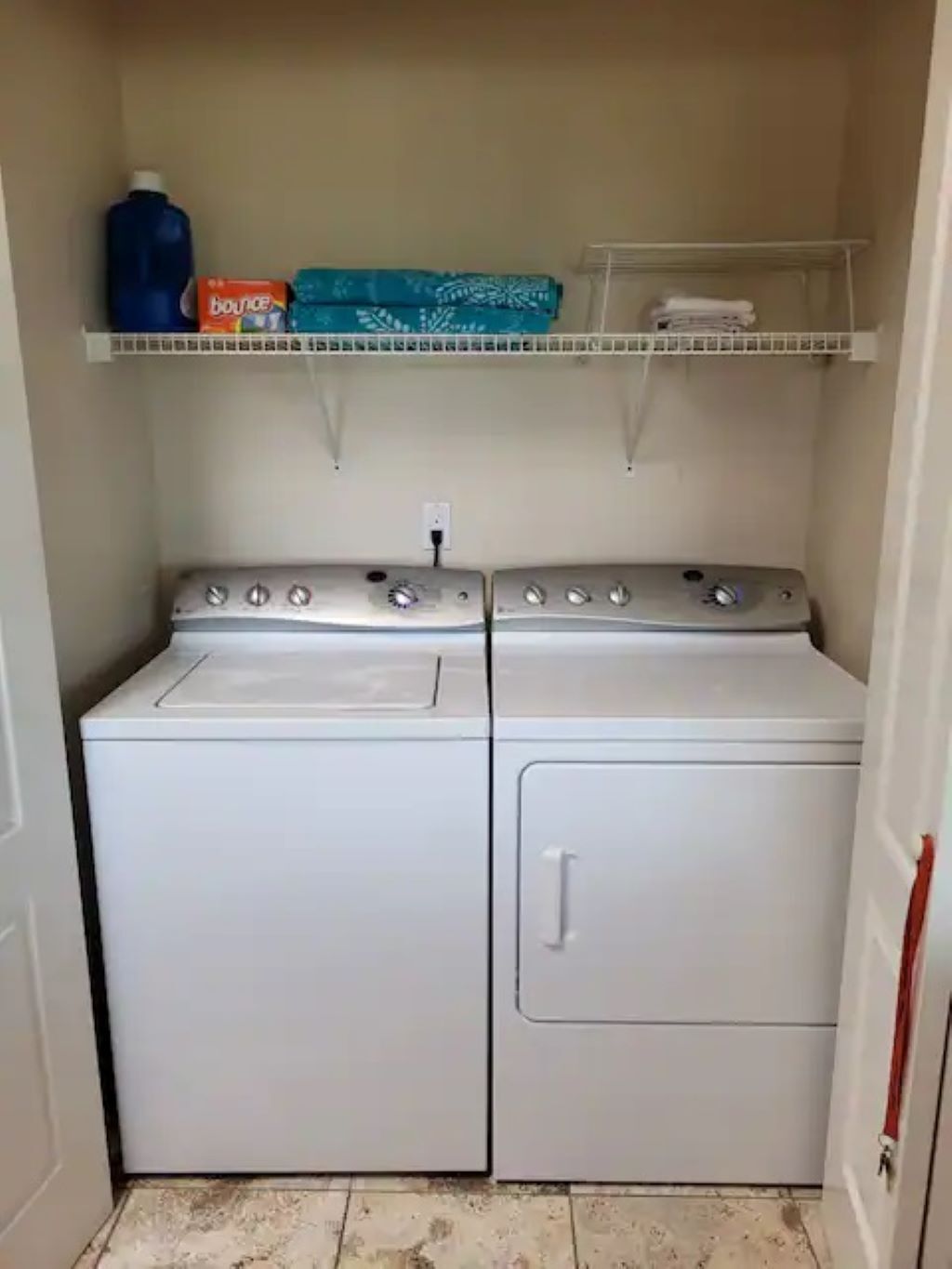 Un cuarto de lavandería con dos lavadoras y secadoras apiladas, un estante con una botella de detergente Bounce y un tendedero.