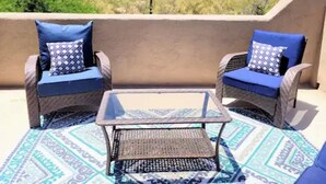 A patio with two wicker chairs and a small table, a patterned rug, and a view of a desert landscape. - Beautiful Mountain Views and a spacious relaxing home in NW Tucson. (Tucson)