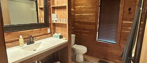 Ein Badezimmer einer Holzhütte mit Waschbecken, Spiegel, Toilette und einem Fenster.