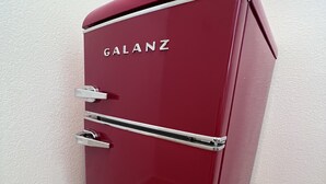 Ein roter Galanz-Kühlschrank steht in einer Ecke, neben einer Wand mit strukturierter Oberfläche und einem Teppichboden.