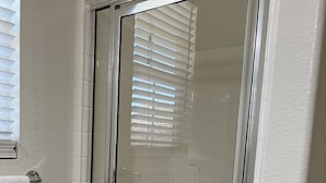 Eine Duschkabine mit Glastrennwand, weißen Fliesen und einem weißen Handtuch an der Wand.
