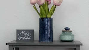 Eine dunkelblaue Vase mit rosa Tulpen auf einem grauen Konsolentisch.