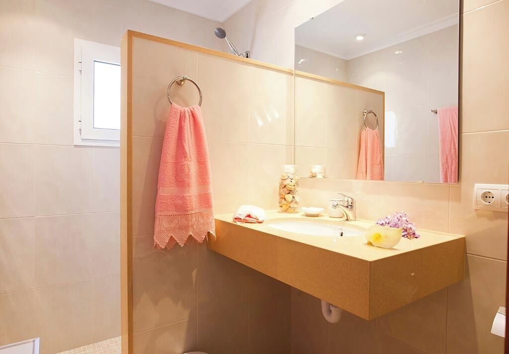 Un baño con pared de azulejos color beige, un lavabo con espejo y dos toallas colgadas en aros.