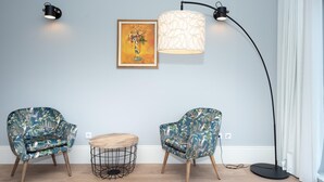 Una stanza con due poltrone a motivi floreali, un tavolo rotondo in legno, una lampada da terra e un quadro appeso al muro.