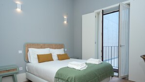 Una camera da letto ordinata con un letto, un comodino, una coperta verde e vista su un balcone attraverso una porta aperta.
