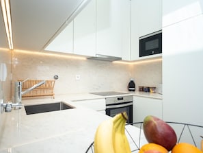 Cozinha moderna com armários brancos, pia de aço inoxidável e forno embutido.