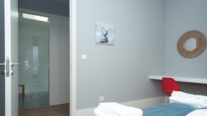 Habitación de hotel con cama, una silla roja, un espejo circular montado en la pared y un cuadro de flores.