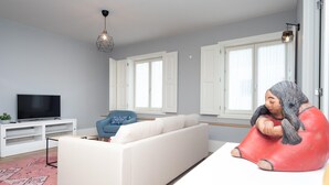 Una sala de estar moderna con un sofá blanco, un sillón azul, un televisor sobre un mueble blanco y una escultura roja.