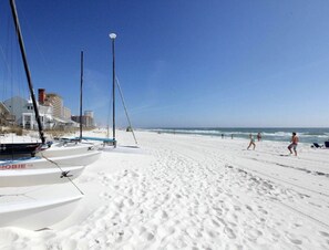 Une plage de sable blanc, quelques personnes et des voiliers.