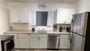 A modern kitchen with white cabinets, a stainless steel refrigerator, and a dishwasher. - Newly remodeled 3b (Panama City Beach)