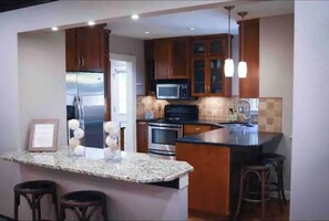 Enjoy cooking in this kitchen with a granite countertop island, bar stools, stainless steel appliances, and wooden cabinetry with glass doors.