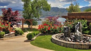 Un jardín ajardinado con fuente, pérgola y vista a un lago con montañas al fondo.