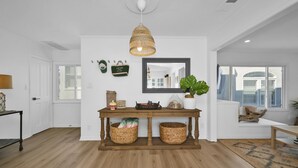 A spacious room with a wooden floor, a central table with baskets, a hanging light fixture, and a large window with a view. - Chic Modern Designed Home w/ Private Studio (Newport Beach)