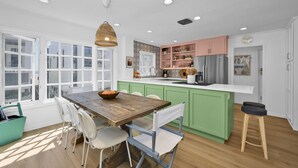A modern kitchen with green cabinets, a wooden dining table, and a hanging light fixture. - Chic Modern Designed Home w/ Private Studio (Newport Beach)