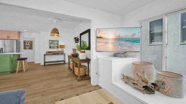 A modern living room with a large TV, a wooden coffee table, and a view of the ocean through a window. - Chic Modern Designed Home w/ Private Studio (Newport Beach)