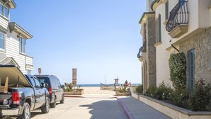 A beachfront street with parked vehicles, a clear sky, and a distant beach view. - Chic Modern Designed Home w/ Private Studio (Newport Beach)