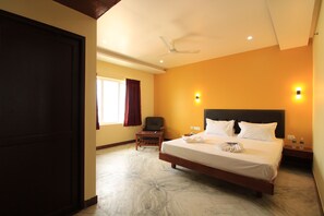 Una habitación de hotel con una cama grande, una silla, un escritorio y un ventilador de techo.