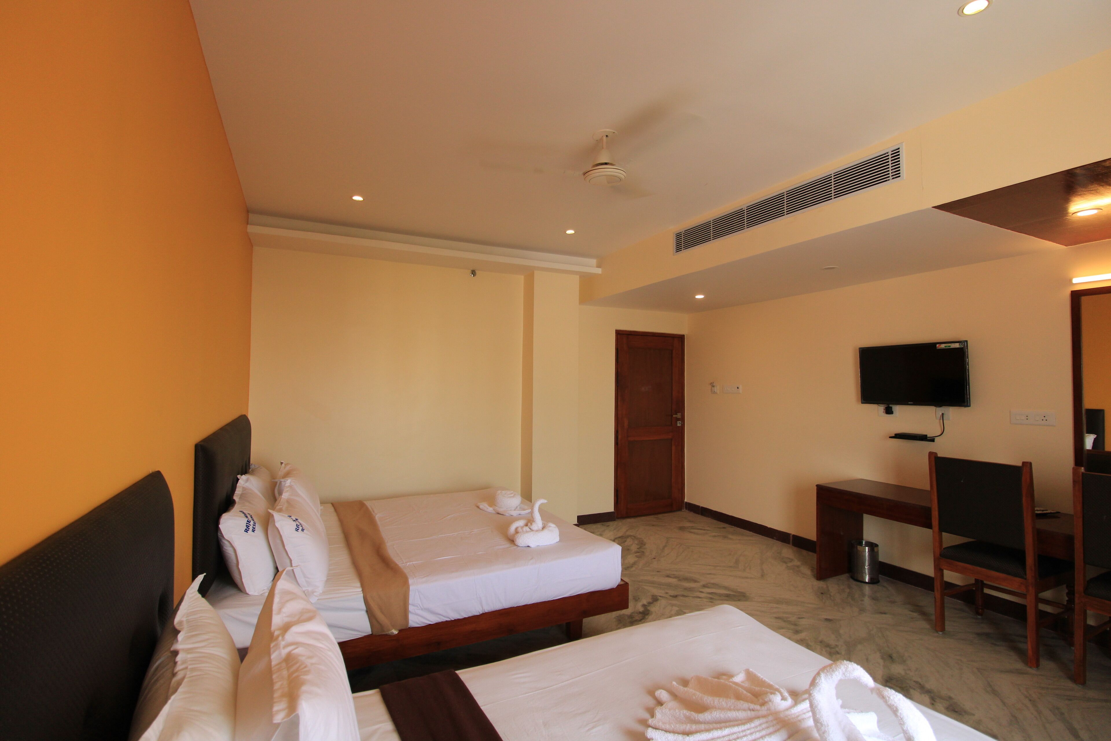 A hotel room with two beds, a desk, a chair, a television, and a door.