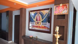 Un espace d’accueil agrémenté d’un tableau religieux encadré, d’une statue et d’un petit autel orné de fleurs et d’encens.