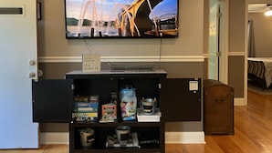 Ett rum med en tv-skärm som visar en bro och ett vattenlandskap, en hylla med böcker och spel samt en dörr som leder till ett annat rum.