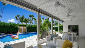 Et moderne udendørs opholdsområde med pool, hvide møbler og udsigt til palmer.