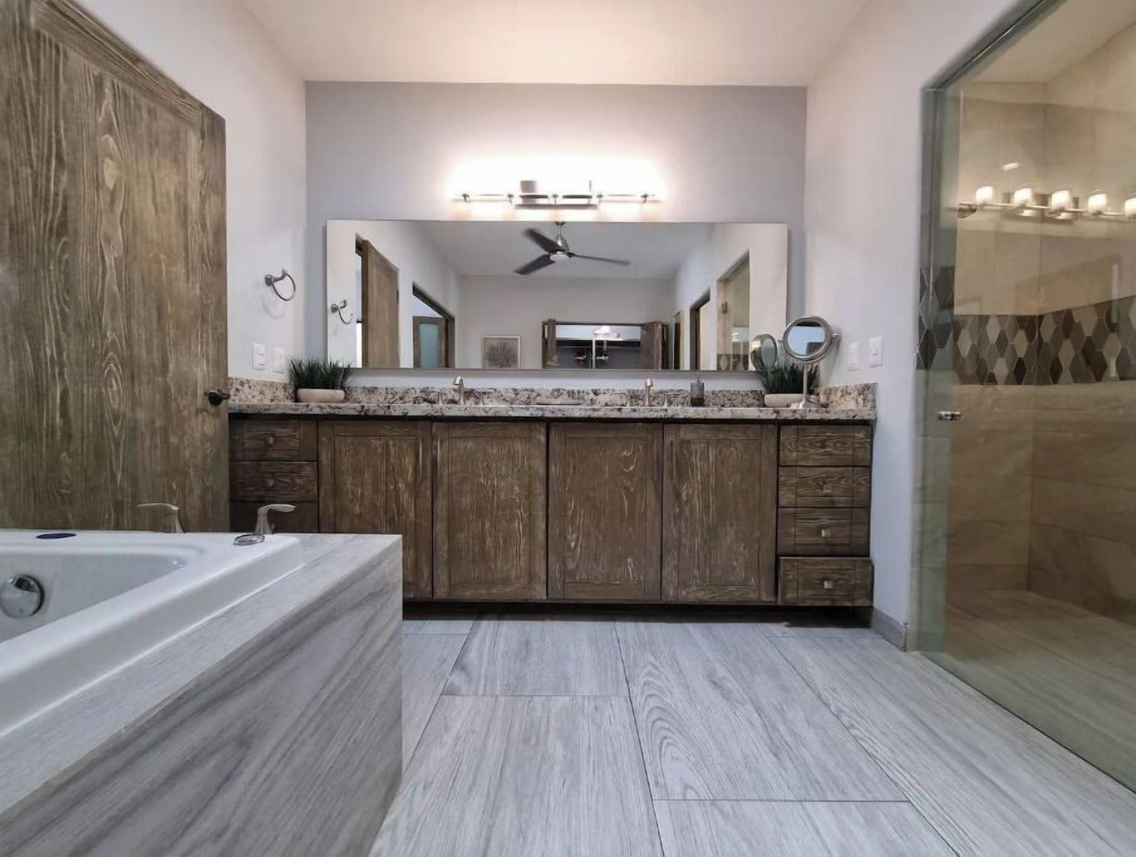 A modern bathroom with a large mirror, wooden cabinets, a bathtub, and a shower area.