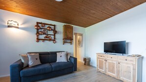 A living room with a dark blue sofa, a wooden cabinet with a flat-screen TV, and a wall-mounted copper cookware rack. - One bedroom Apartment in Canazei (Campitello di Fassa)