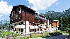 A multi-story building with balconies, a paved area in front, and a mountainous backdrop. - One bedroom Apartment in Canazei (Campitello di Fassa)