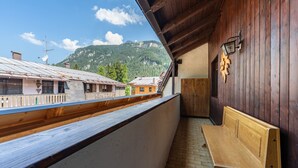 A wooden balcony with a bench, a wooden wall, and a view of buildings and mountains. - One bedroom Apartment in Canazei (Campitello di Fassa)