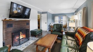 Ein Wohnzimmer mit Kamin, Ledermöbeln, einem Fernseher und Blick ins Freie.
