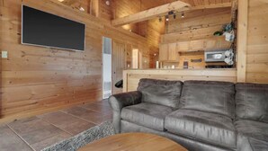 Interno di una baita in legno con un divano in pelle, una televisione a schermo piatto e un angolo cottura.