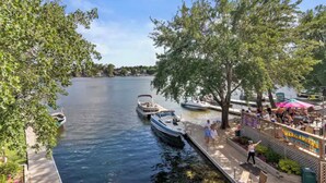 Un molo lungo il fiume con barche, un ristorante con tavoli all'aperto e alberi che costeggiano l'acqua.