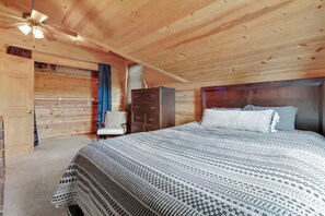 Ein Schlafzimmer einer Holzhütte mit Bett, Schminktisch und Deckenventilator.