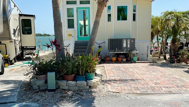 A single-story house with a green door, a porch, and a small garden with potted plants.