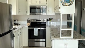 A modern kitchen with white cabinets, stainless steel appliances, and a marble countertop.